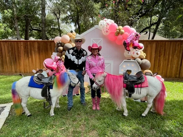 Cowboy Mike and Cowgirl Marian with two colorful ponies at a birthday celebration